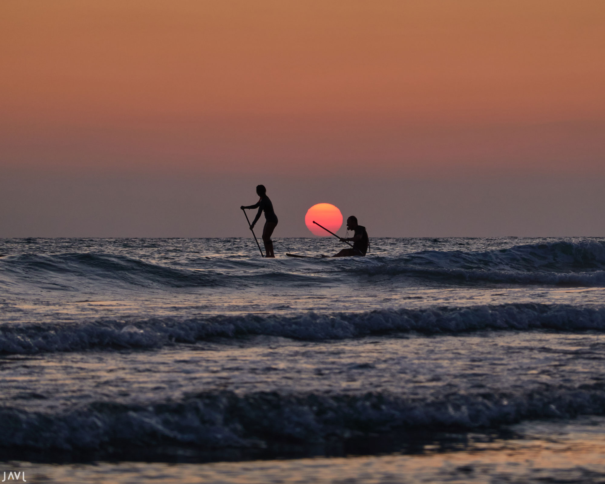 Dos personas practican paddle surf durante la puesta de sol en El Palmar