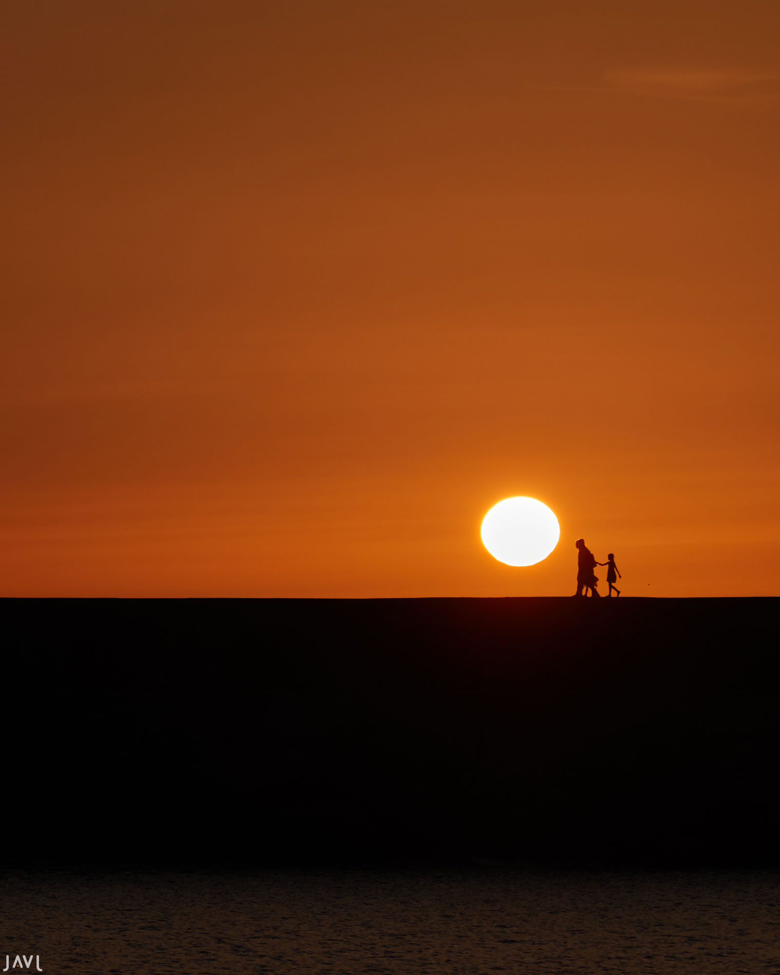 Una familia pasea por el rompeolas de la playa de Tazacorte en la puesta de sol